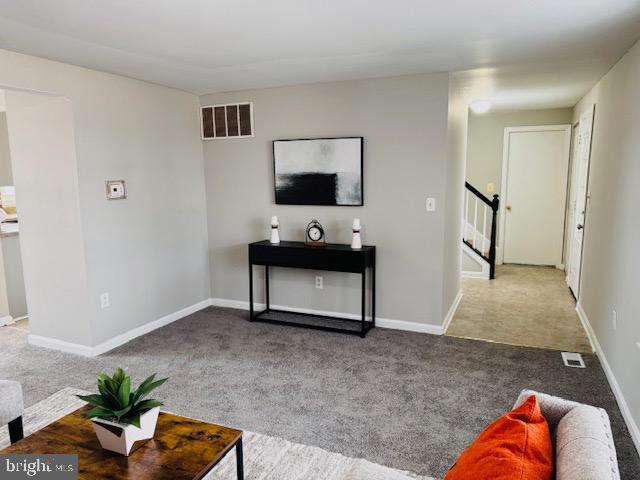 living room featuring carpet floors, stairway, baseboards, and visible vents