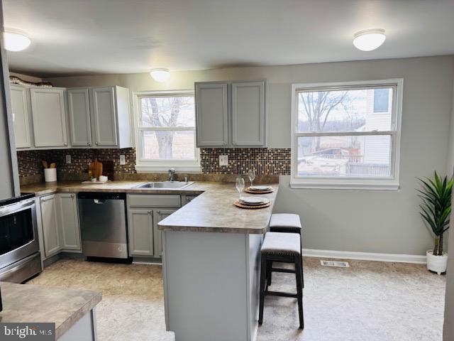 kitchen with a breakfast bar area, gray cabinets, appliances with stainless steel finishes, a sink, and a peninsula