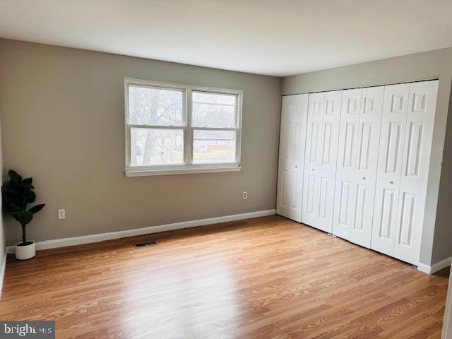 unfurnished bedroom with a closet, light wood-type flooring, visible vents, and baseboards