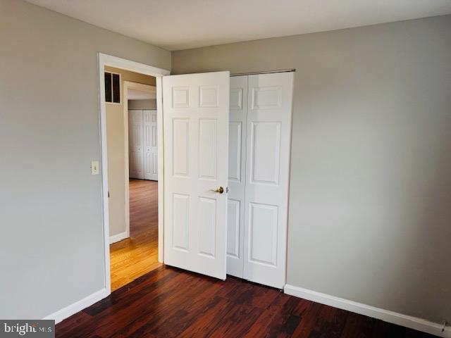 unfurnished bedroom with visible vents, a closet, baseboards, and dark wood-type flooring