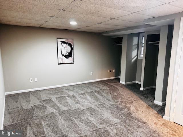 finished basement with carpet, a paneled ceiling, and baseboards