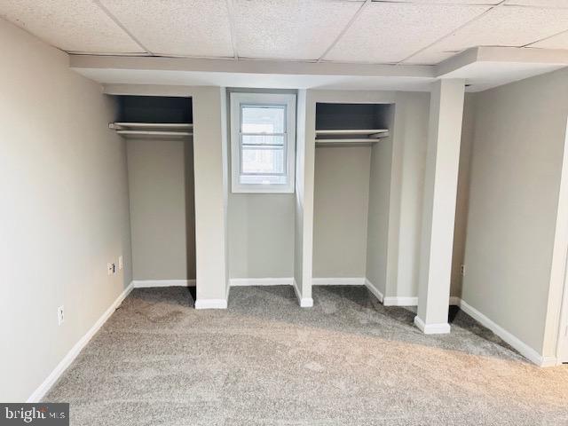 unfurnished bedroom featuring a paneled ceiling, carpet, baseboards, and multiple closets