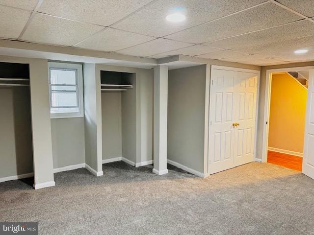 unfurnished bedroom featuring baseboards, a drop ceiling, multiple closets, and carpet flooring