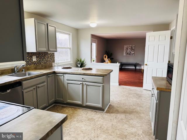 kitchen with gray cabinets, a sink, a peninsula, and stainless steel dishwasher