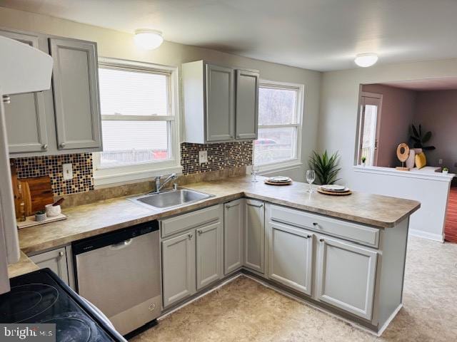 kitchen featuring a peninsula, a sink, stainless steel dishwasher, gray cabinets, and backsplash