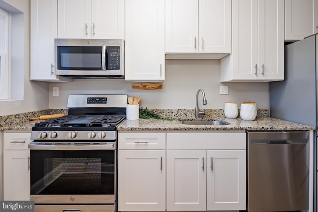 kitchen with white cabinets, light stone counters, stainless steel appliances, and a sink