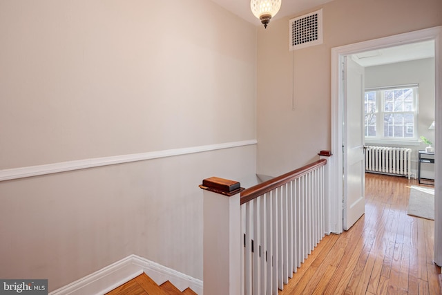 staircase with baseboards, radiator heating unit, visible vents, and hardwood / wood-style flooring