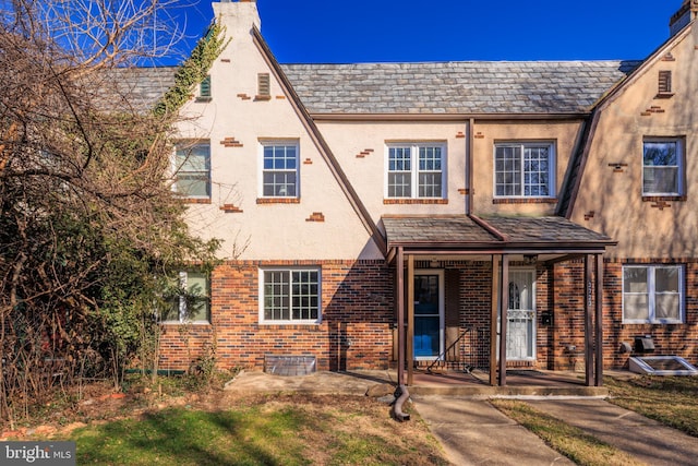 view of front of home featuring brick siding, a high end roof, a porch, stucco siding, and a chimney