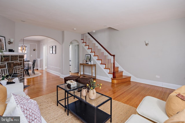 living room featuring arched walkways, stairway, wood finished floors, and baseboards