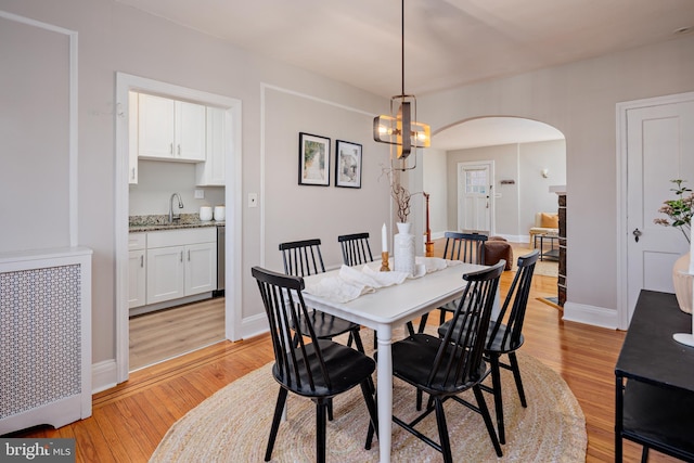 dining space with arched walkways, radiator, baseboards, and light wood finished floors