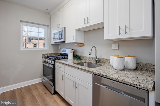 kitchen featuring light wood-style flooring, appliances with stainless steel finishes, white cabinets, a sink, and baseboards