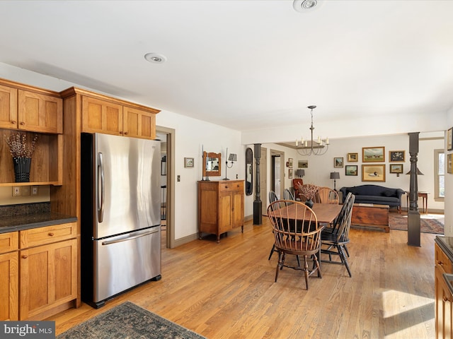 kitchen with dark countertops, light wood-type flooring, freestanding refrigerator, an inviting chandelier, and brown cabinetry