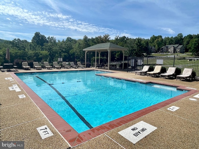 community pool with a patio area, fence, and a gazebo