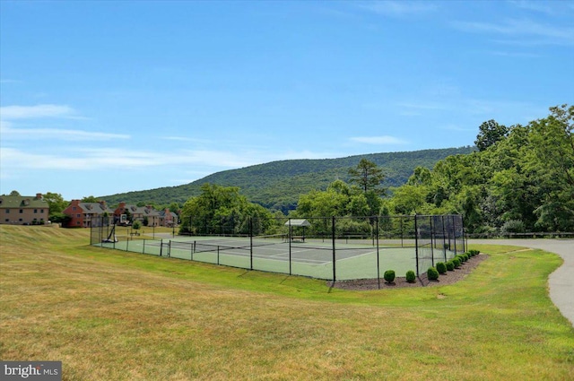 view of tennis court featuring fence, a mountain view, and a yard