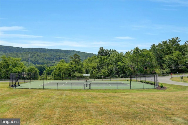 view of sport court with a yard, a view of trees, and fence