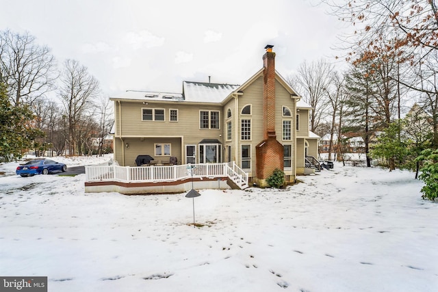 snow covered property with a chimney and a wooden deck