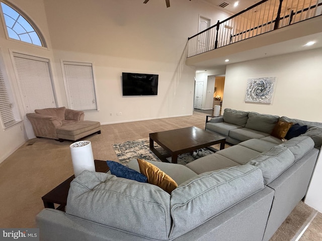 living area with visible vents, baseboards, a ceiling fan, a towering ceiling, and carpet