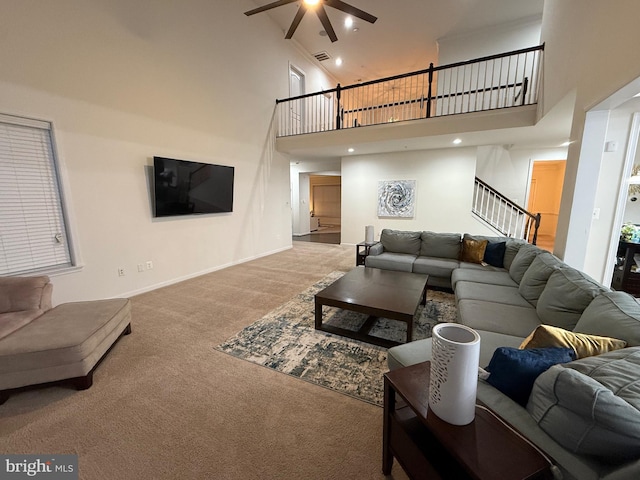 carpeted living area with a high ceiling, visible vents, a ceiling fan, baseboards, and stairway