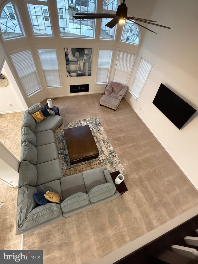 carpeted living room featuring a ceiling fan and a high ceiling