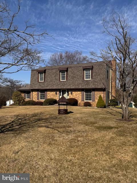 view of front of home featuring a chimney, brick siding, roof with shingles, and a front lawn