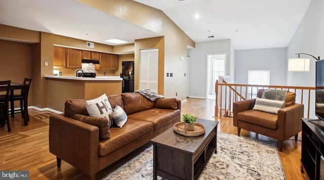 living room with visible vents, lofted ceiling, baseboards, and light wood finished floors