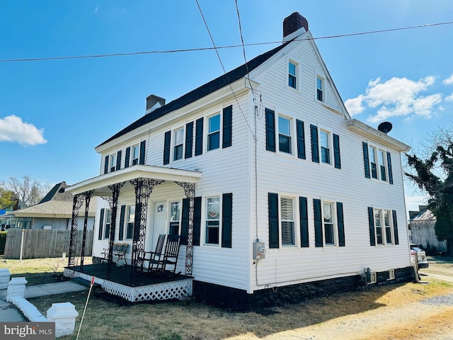 view of home's exterior featuring a chimney, covered porch, and fence