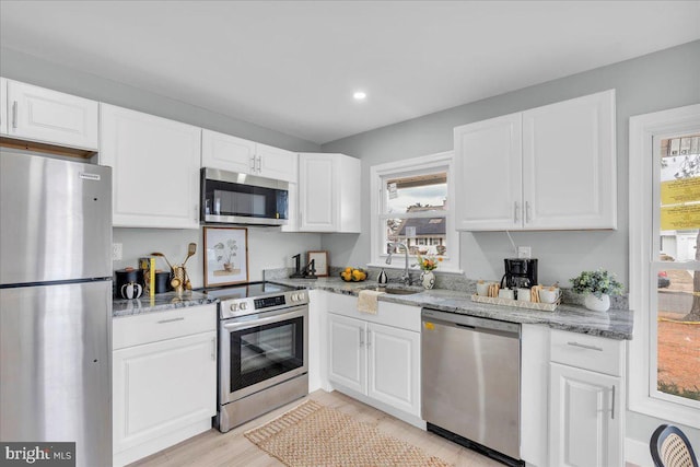 kitchen featuring light stone counters, white cabinetry, stainless steel appliances, and a sink