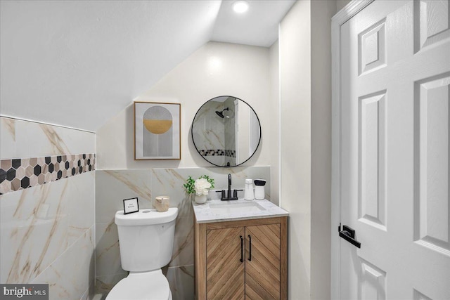 bathroom with tile walls, vaulted ceiling, vanity, and toilet