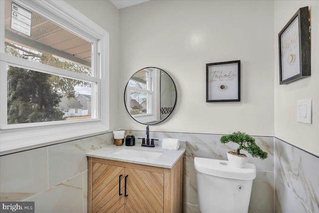 bathroom featuring toilet, wainscoting, vanity, and tile walls