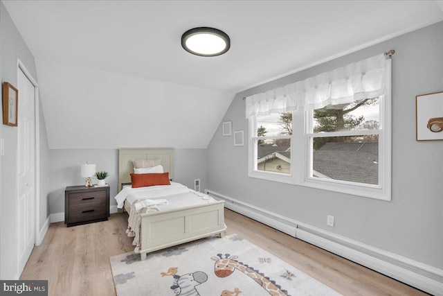 bedroom featuring lofted ceiling, light wood-style floors, baseboards, and a baseboard heating unit