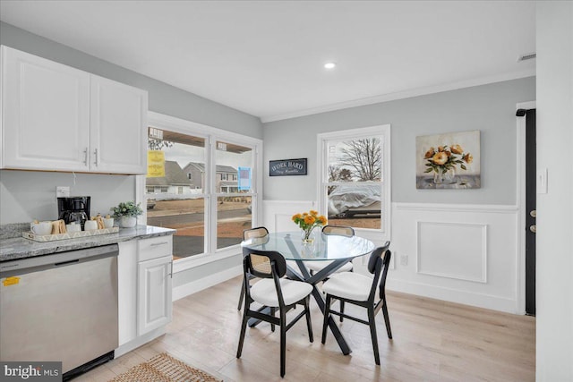 dining area featuring light wood-type flooring, a wainscoted wall, visible vents, and crown molding