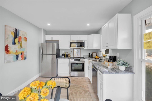 kitchen with baseboards, light stone countertops, stainless steel appliances, white cabinetry, and a sink