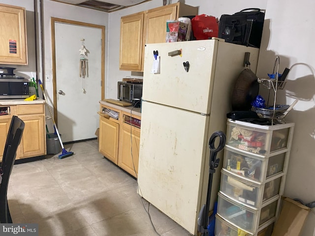 kitchen featuring light countertops, light brown cabinetry, stainless steel microwave, and freestanding refrigerator