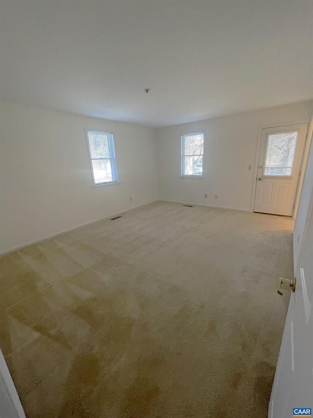 unfurnished room with baseboards, a wealth of natural light, and light colored carpet