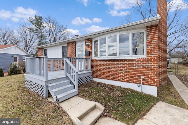 view of front of home featuring a chimney, fence, a wooden deck, a front lawn, and brick siding