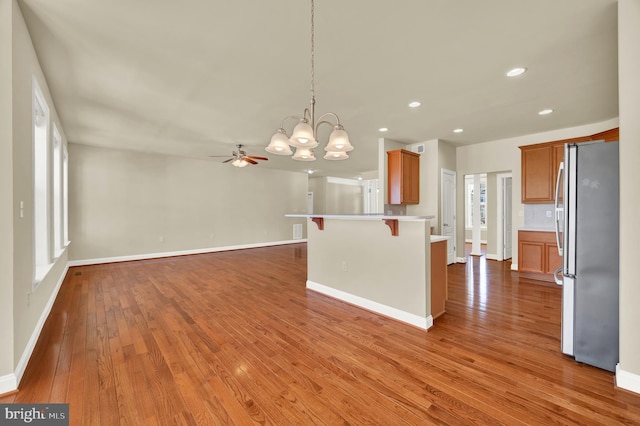 kitchen with a breakfast bar, freestanding refrigerator, wood-type flooring, and a peninsula