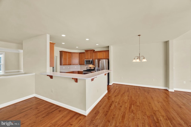 kitchen featuring appliances with stainless steel finishes, brown cabinetry, light wood-style floors, a peninsula, and a kitchen bar