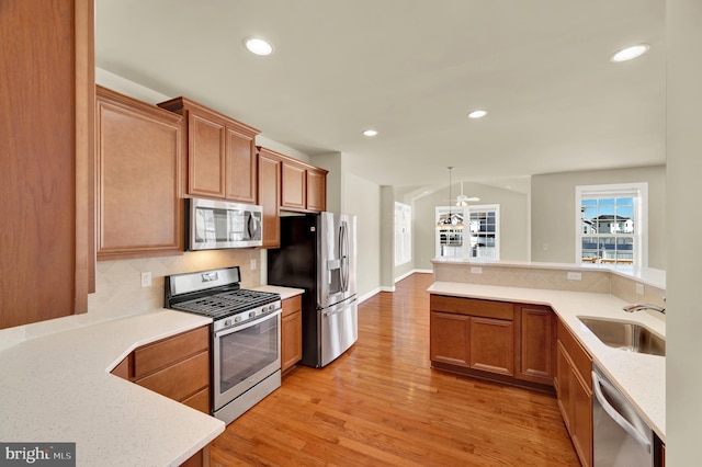 kitchen featuring tasteful backsplash, light wood-style flooring, brown cabinets, stainless steel appliances, and a sink