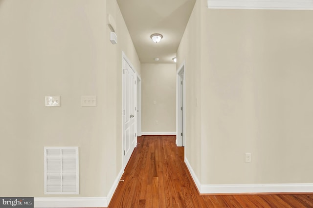 hall featuring wood finished floors, visible vents, and baseboards