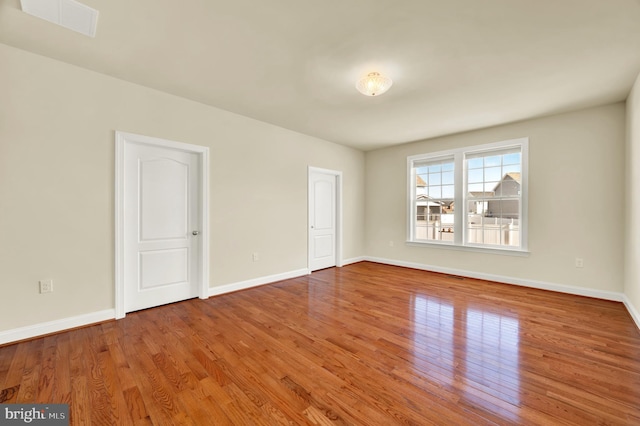 spare room with wood finished floors, visible vents, and baseboards