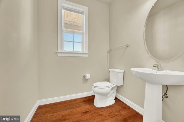 half bath with toilet, baseboards, and wood finished floors