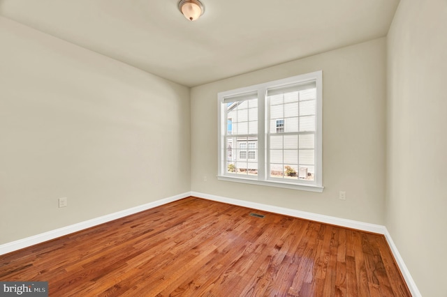 spare room with baseboards, visible vents, and wood finished floors