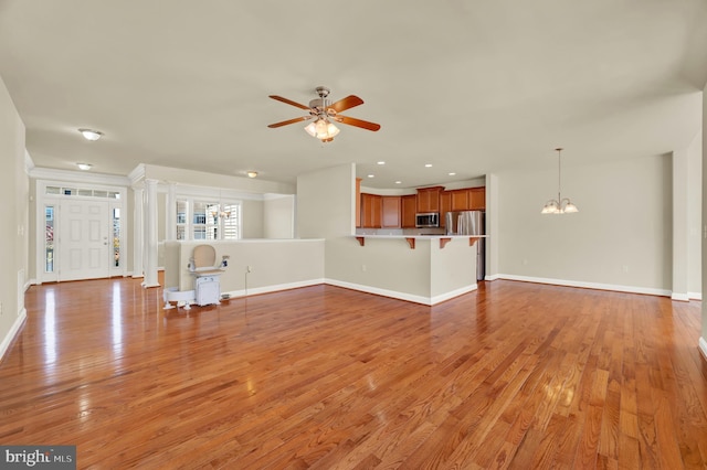 unfurnished living room with baseboards, ornate columns, ceiling fan with notable chandelier, light wood-style floors, and recessed lighting