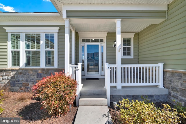 view of exterior entry with stone siding and covered porch