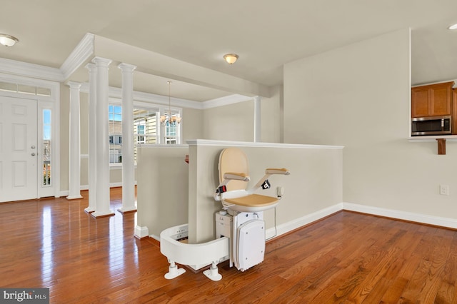 sitting room featuring baseboards, wood finished floors, crown molding, ornate columns, and a chandelier