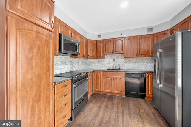 kitchen with dark wood-style floors, dark stone countertops, a sink, black appliances, and backsplash