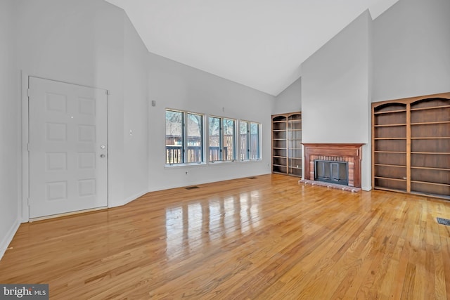 unfurnished living room with high vaulted ceiling, a fireplace, wood finished floors, and visible vents