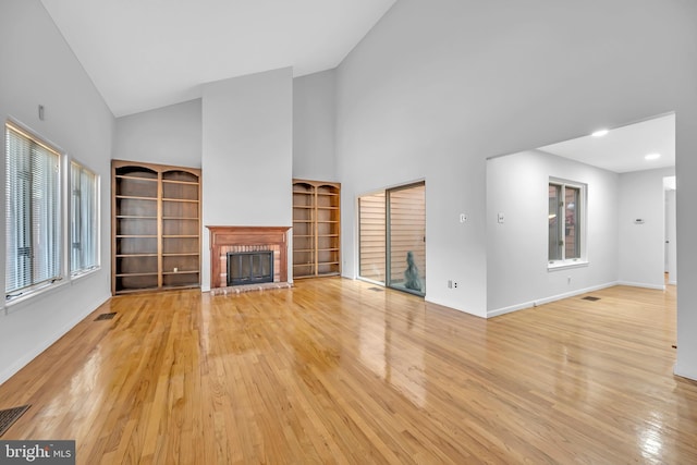 unfurnished living room featuring light wood-style floors, a fireplace, visible vents, and high vaulted ceiling