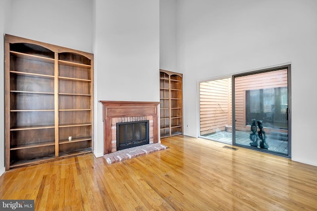 unfurnished living room with a brick fireplace, visible vents, a high ceiling, and wood finished floors