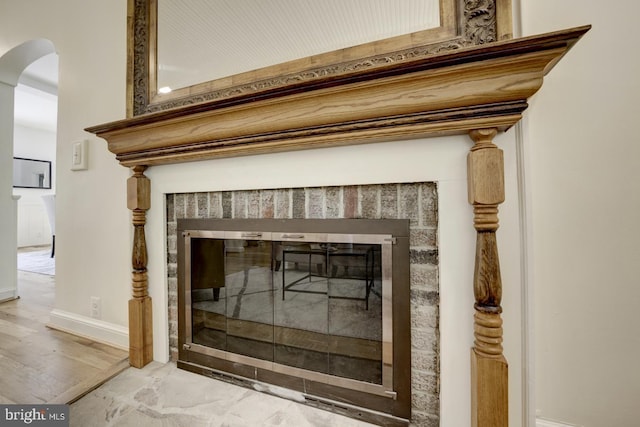 room details featuring baseboards, arched walkways, a brick fireplace, and wood finished floors